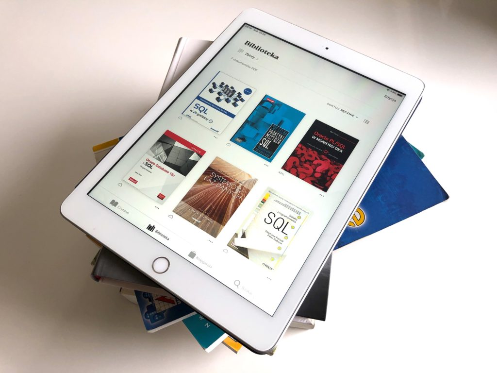 Stos książek i tablet z zainstalowaną biblioteką ebooków